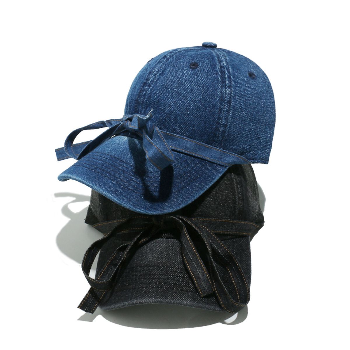 Washed denim baseball cap with a curved brim, seamed crown, top button, ventilation eyelets, and an oversized front bow with trailing ends.