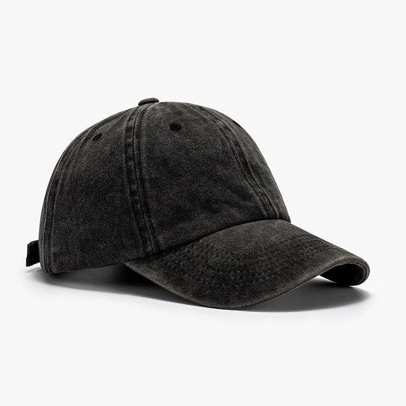 Washed black cotton baseball cap with a relaxed rounded crown, visible panel seams, crown button, ventilation eyelets, and a distinctly curved brim.