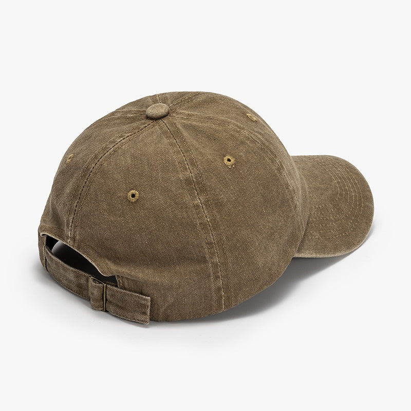 Washed brown cotton baseball cap with a relaxed rounded crown, curved brim, visible panel seams, ventilation eyelets, and an adjustable back buckle strap.
