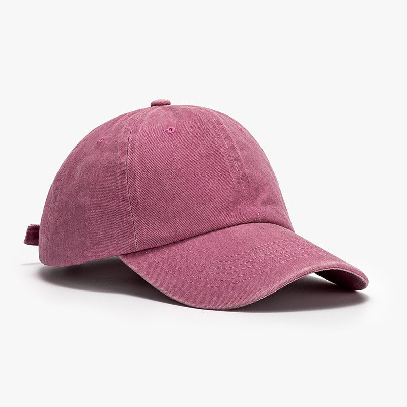 Washed mauve cotton baseball cap with a relaxed rounded crown, curved brim, visible panel seams, stitched brim, ventilation eyelets, and top button.