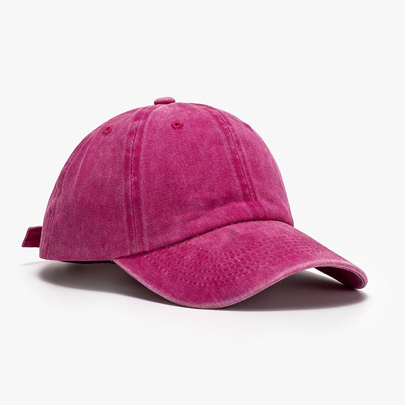 Washed magenta cotton baseball cap with a relaxed rounded crown, visible panel seams, stitched curved brim, ventilation eyelets, and top button.