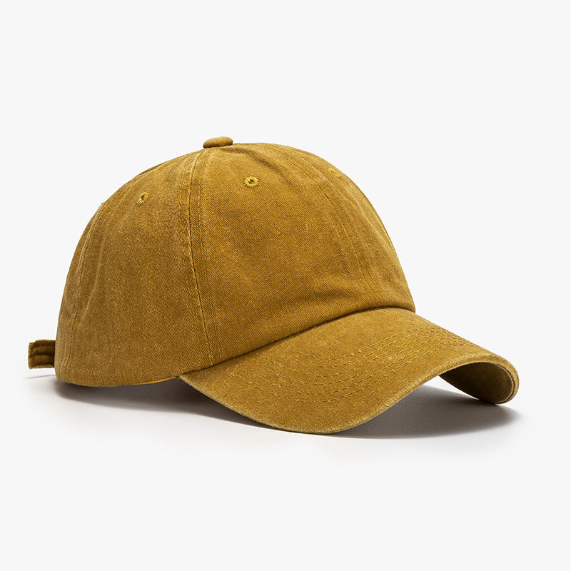 Washed mustard cotton baseball cap with a relaxed rounded crown, curved stitched brim, visible panel seams, ventilation eyelets, and top button.