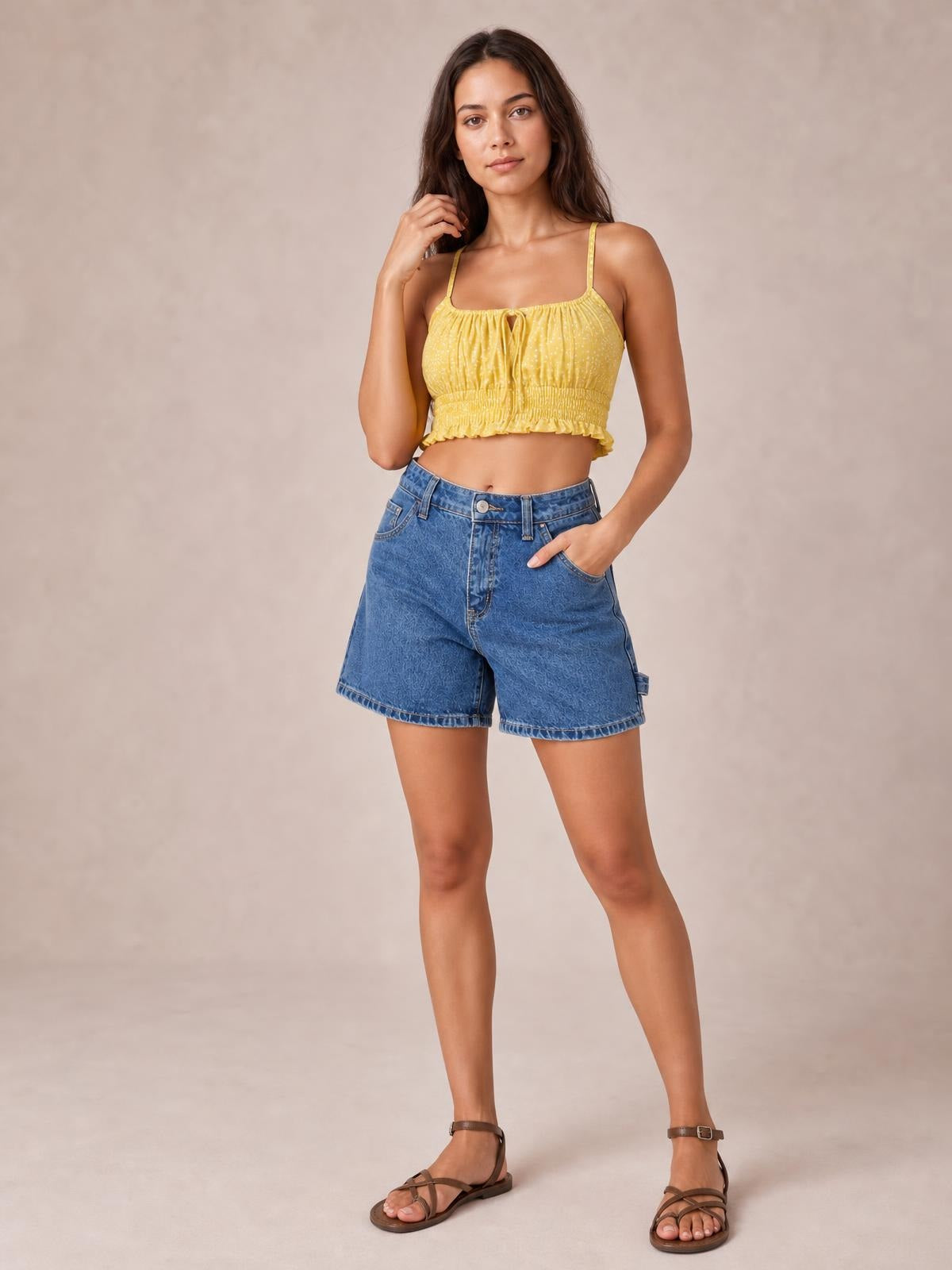 Model poses with one hand in a pocket, wearing washed blue high-rise denim shorts with a relaxed straight-leg silhouette, belt loops, button fly, and side pockets.