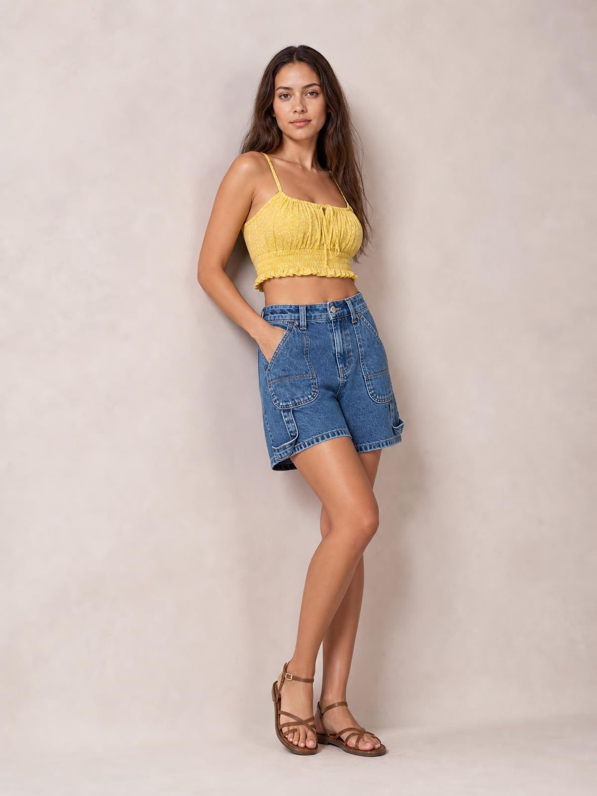 Model poses with one hand in the pocket, wearing washed blue high-rise denim shorts with a structured fit, large front pockets, and rolled cuffs.