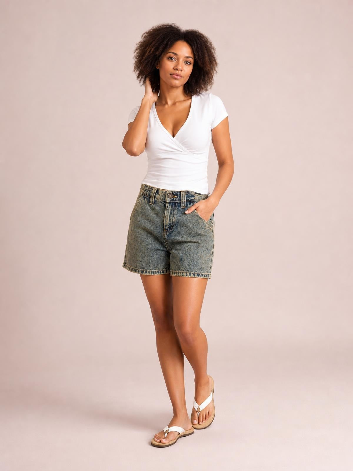 Model wears washed high-rise denim shorts in faded blue with belt loops, button fly, front pockets, a relaxed straight silhouette, and knee-length hems.