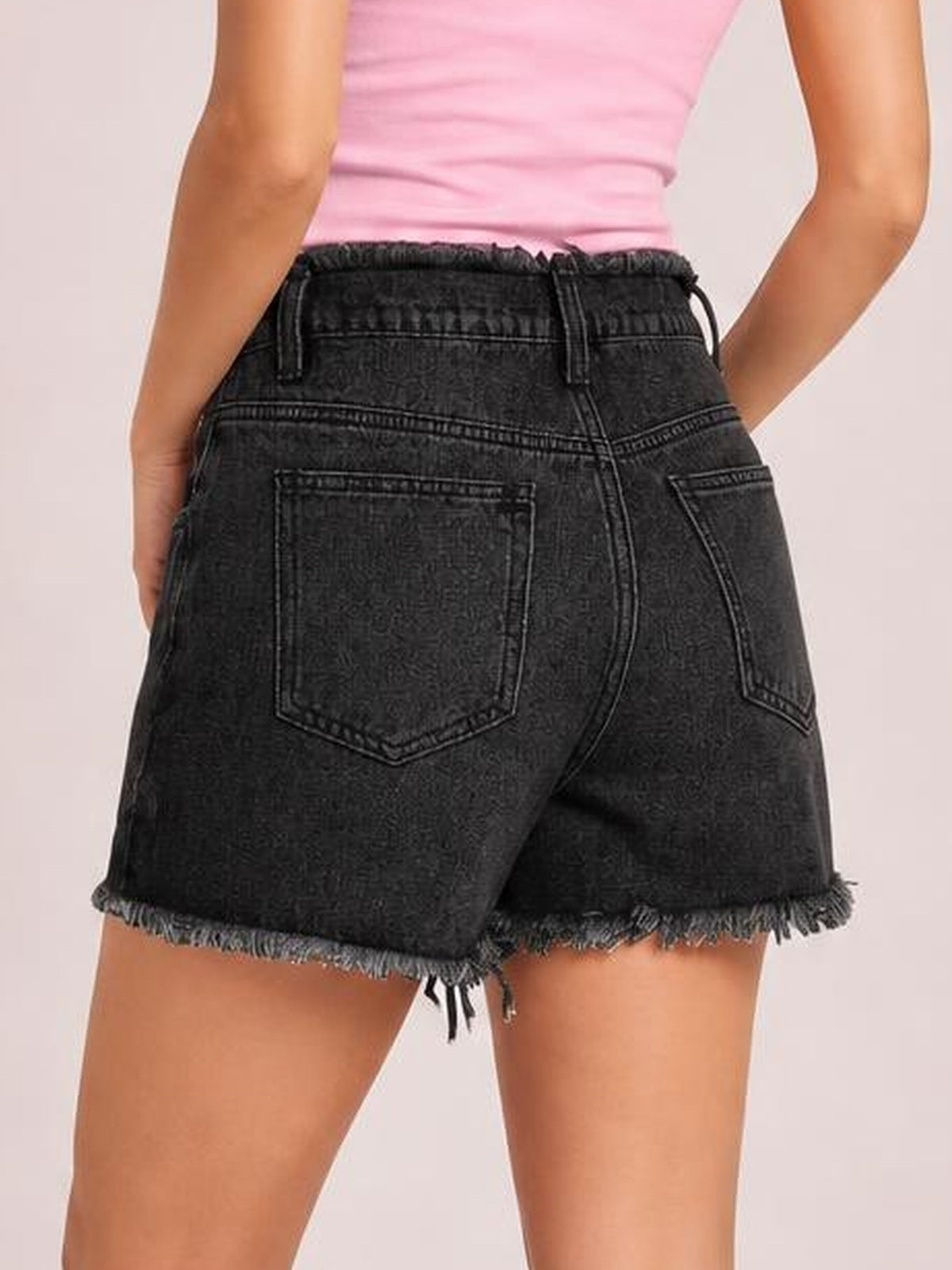 Model shown from the back wearing washed black denim shorts with a relaxed silhouette, drawstring waist, stitched pockets, and raw frayed hems.
