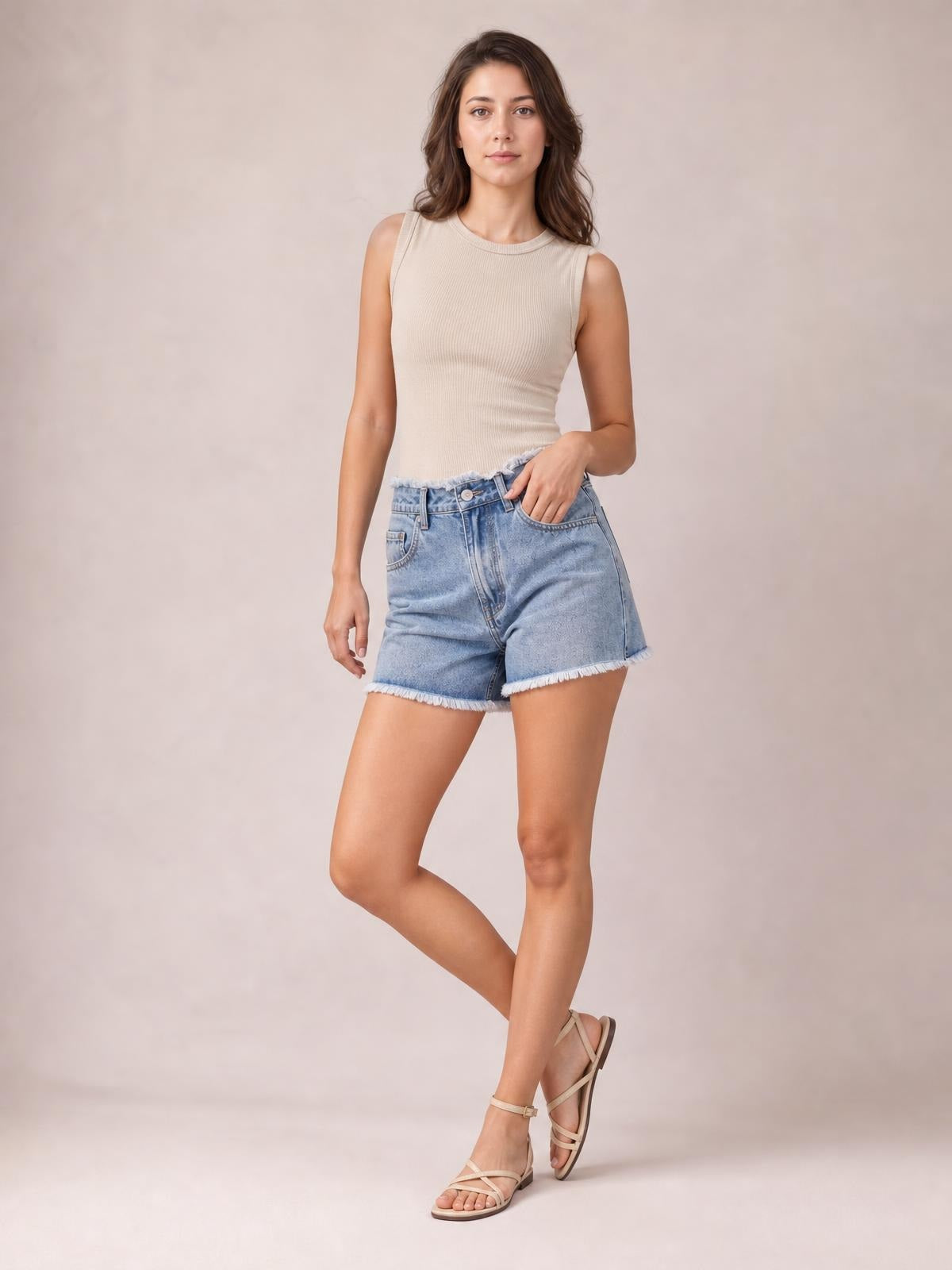 Model poses in light blue washed denim shorts with a raw hem, high-rise silhouette, front pockets, and a button closure.