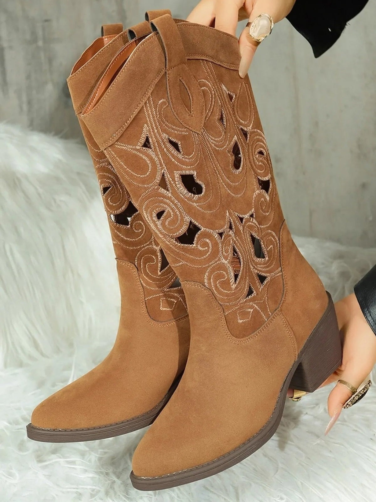 Brown Western cutout pattern boots feature embroidered swirls, pull tabs, pointed toes, mid-height block heels, and a tall suede-look shaft.