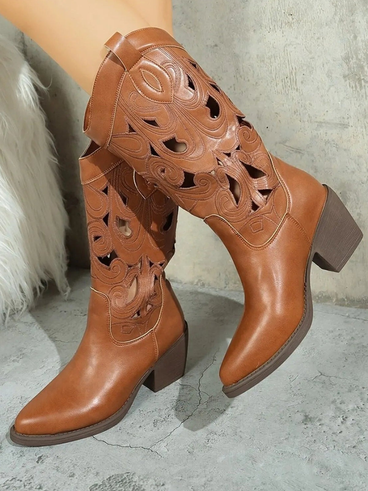 Brown Western cutout pattern boots with pointed toes, stitched swirls, decorative perforations, mid block heels, and tall fitted shafts.