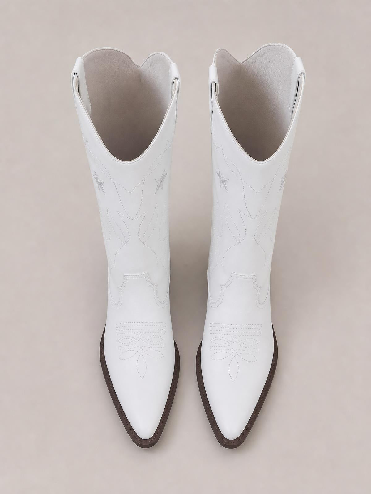 Pair of white Western cowboy boots with star embroidery, stitched floral detailing, pointed toes, scalloped shafts, and contrasting brown rubber soles.