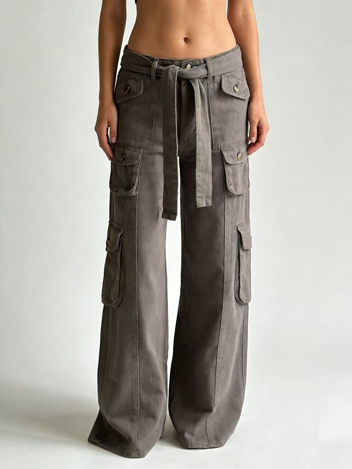 Model stands facing forward in gray wide-leg cargo jeans with multiple flap pockets, a tied waist belt, and a relaxed full-length silhouette.