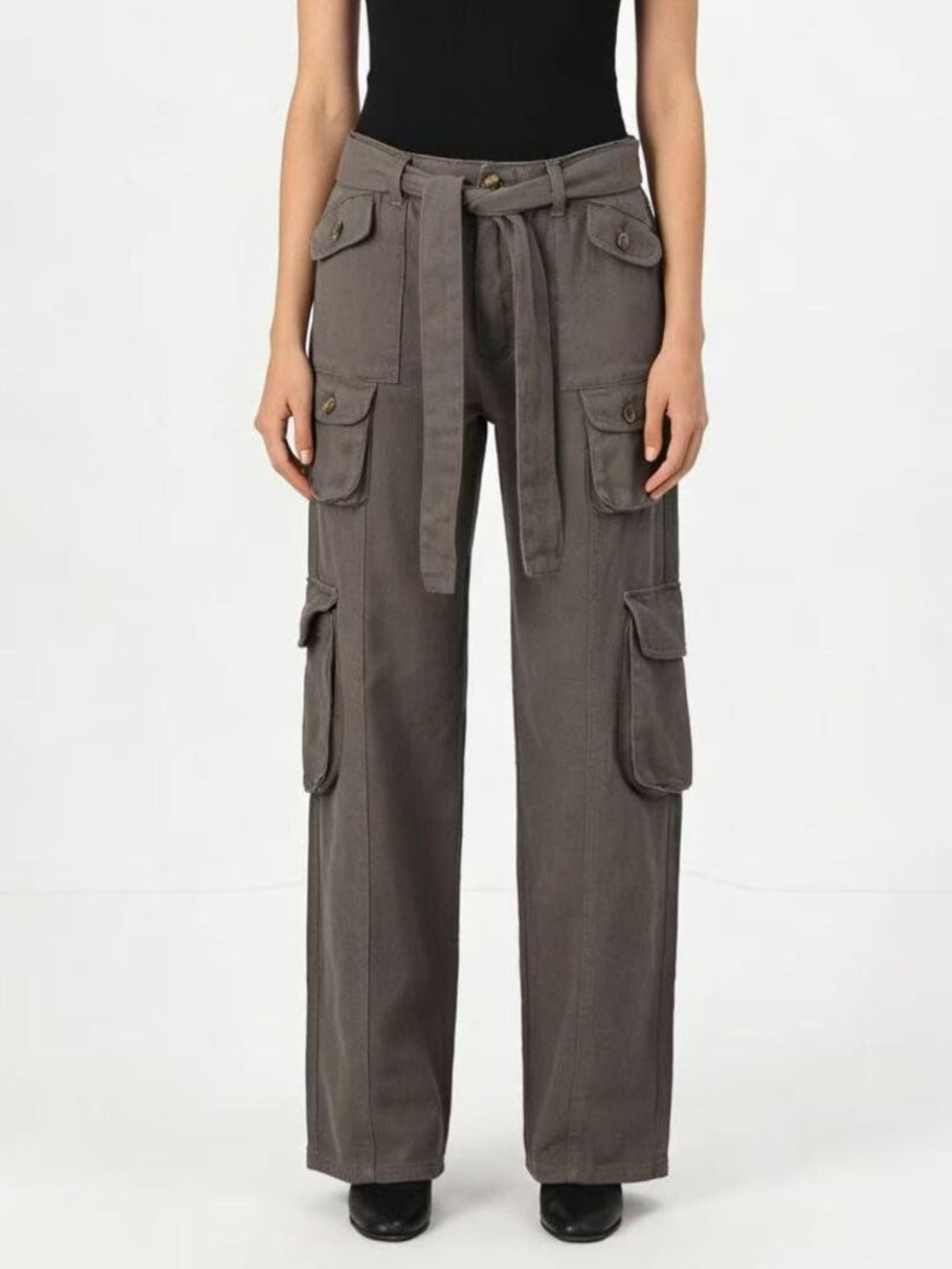 Model wears gray wide-leg cargo jeans with multiple flap pockets, a high waist, and a tied belt, standing front-facing with arms at her sides.