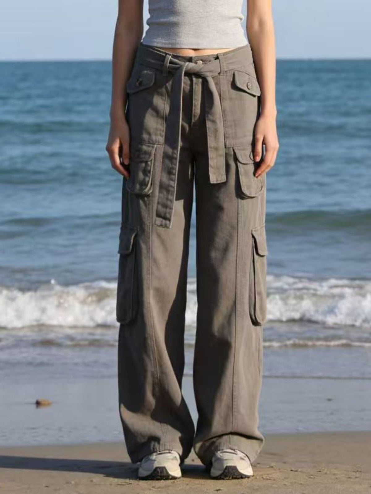 Model stands wearing taupe wide-leg cargo jeans with a tied waist, multiple flap pockets, and a relaxed full-length silhouette.