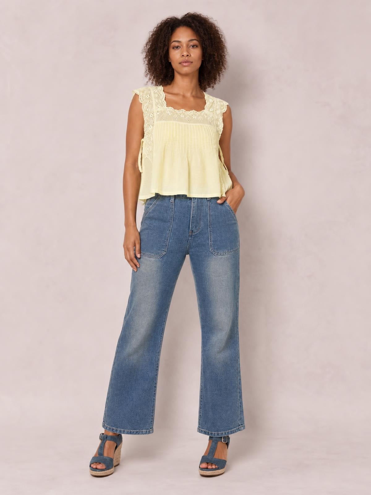 A model poses in blue wide-leg jeans with contrasting white stitching, a high waist, large front patch pockets, and full-length hems, one hand in a pocket.