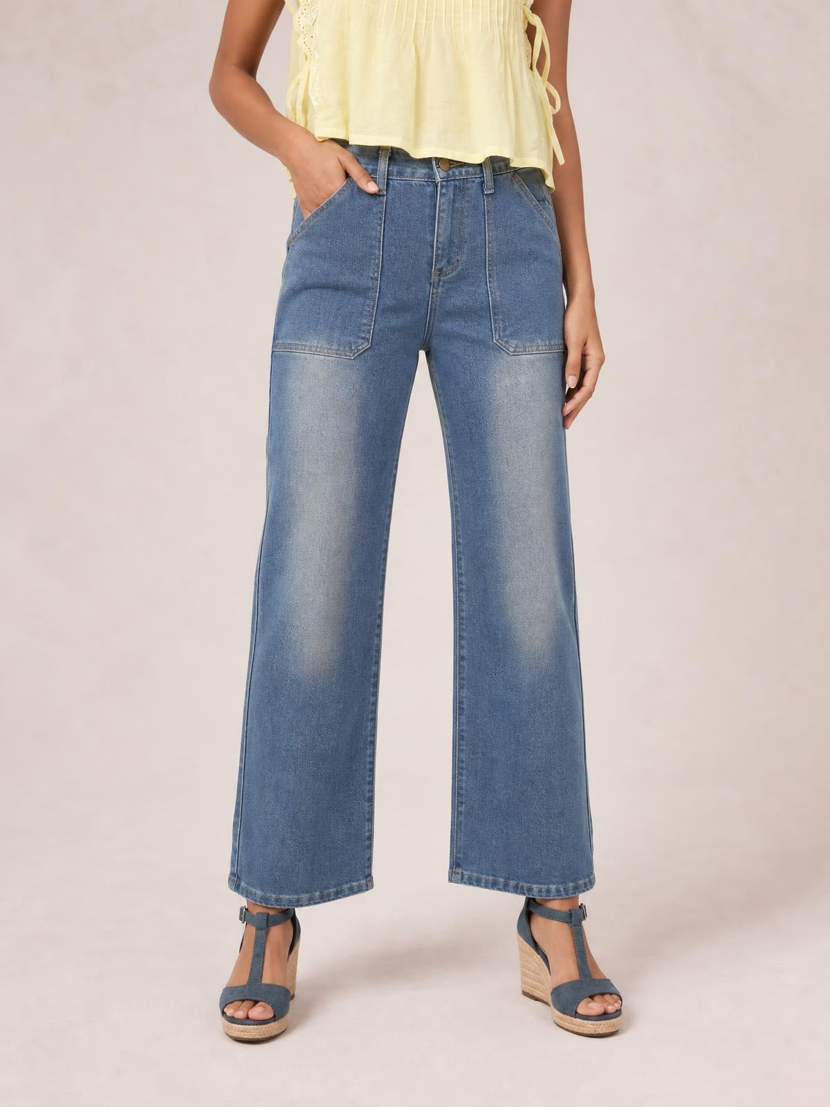 A model stands in blue wide-leg contrast stitching jeans with front patch pockets, belt loops, a button fly, and one hand tucked into a pocket.