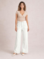 Model standing in white wide-leg jeans with contrast stitching, a high waist, front patch pockets, belt loops, and structured seamed legs.