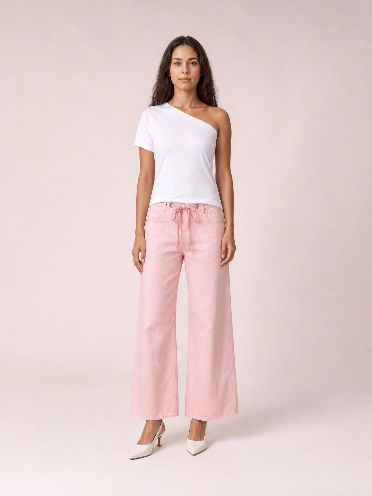 Model stands facing forward in pink wide-leg drawstring jeans with a tied waist, front pockets, seam details, and a cropped full-length silhouette.
