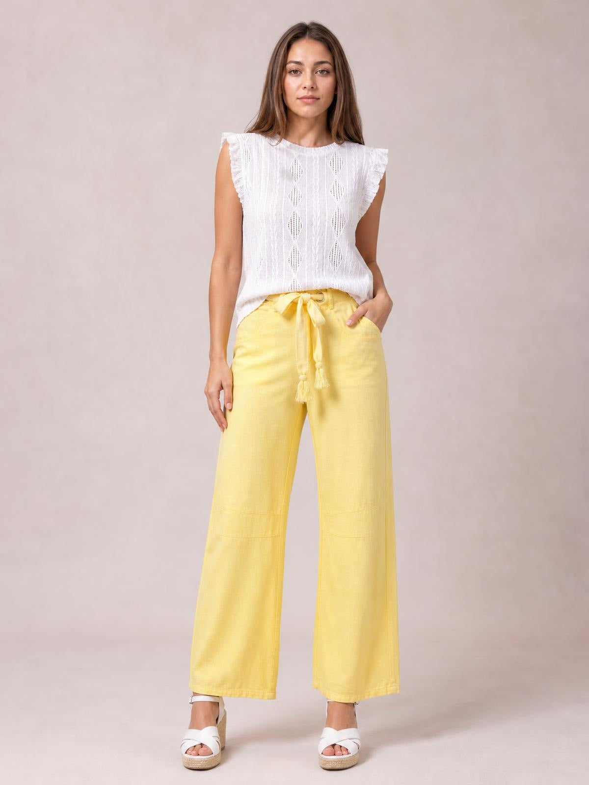 A model stands in bright yellow wide-leg drawstring jeans with a tied waist, visible side pockets, straight seams, and a relaxed ankle-length silhouette.