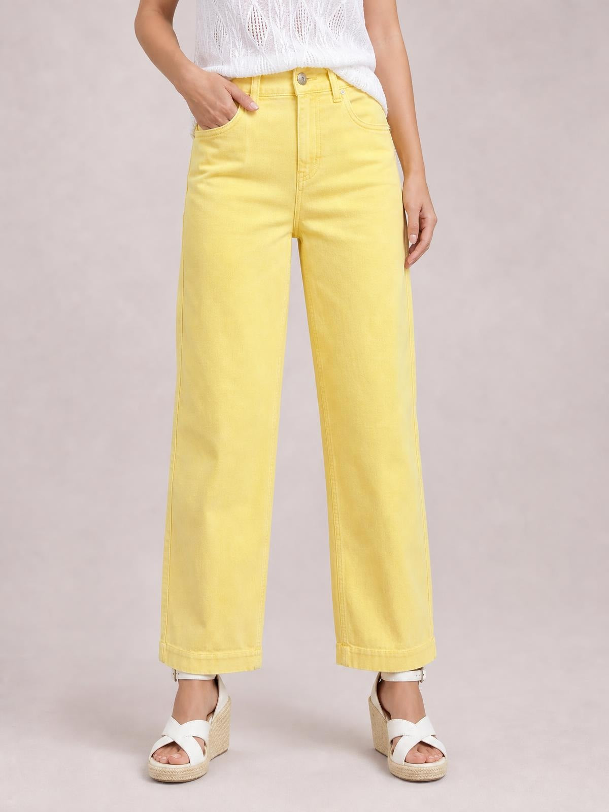 A model wears sunny yellow wide-leg jeans with front pockets, belt loops, button closure, and a relaxed full-length silhouette, posing with one hand in a pocket.