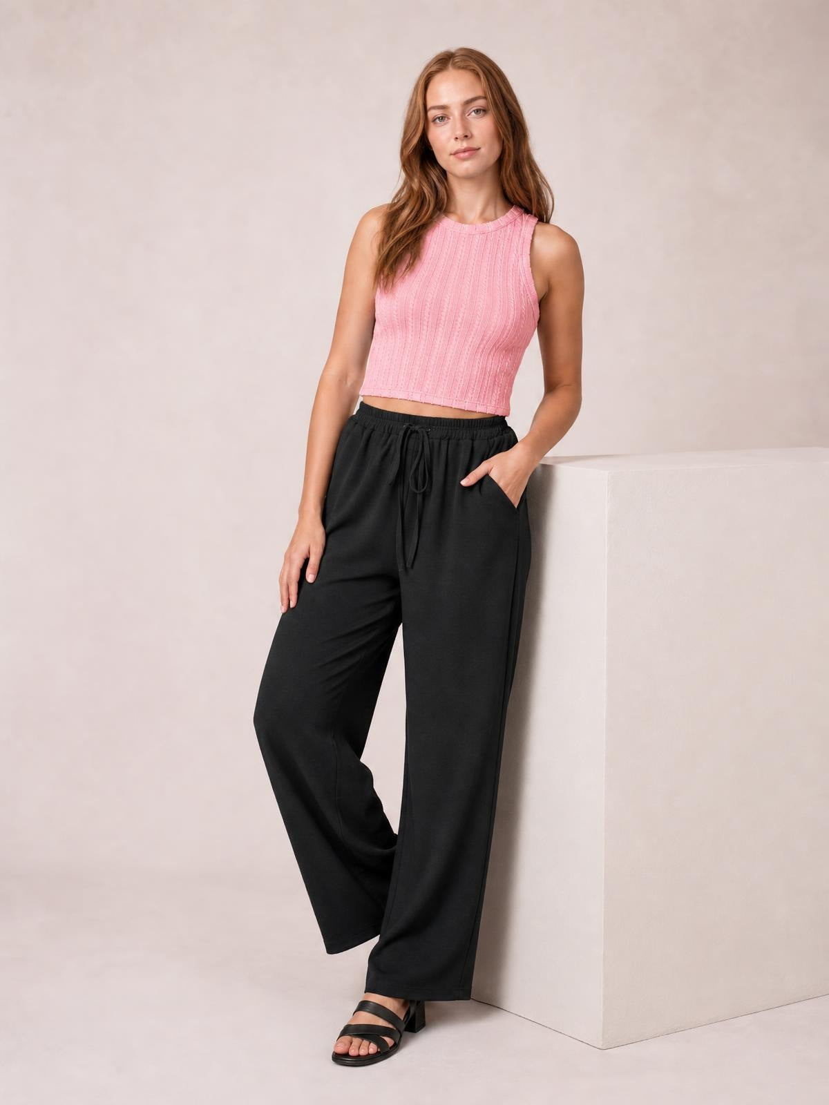 Model poses in black wide leg drawstring pants with a relaxed flowy silhouette, elastic waistband, front tie, and side pockets.
