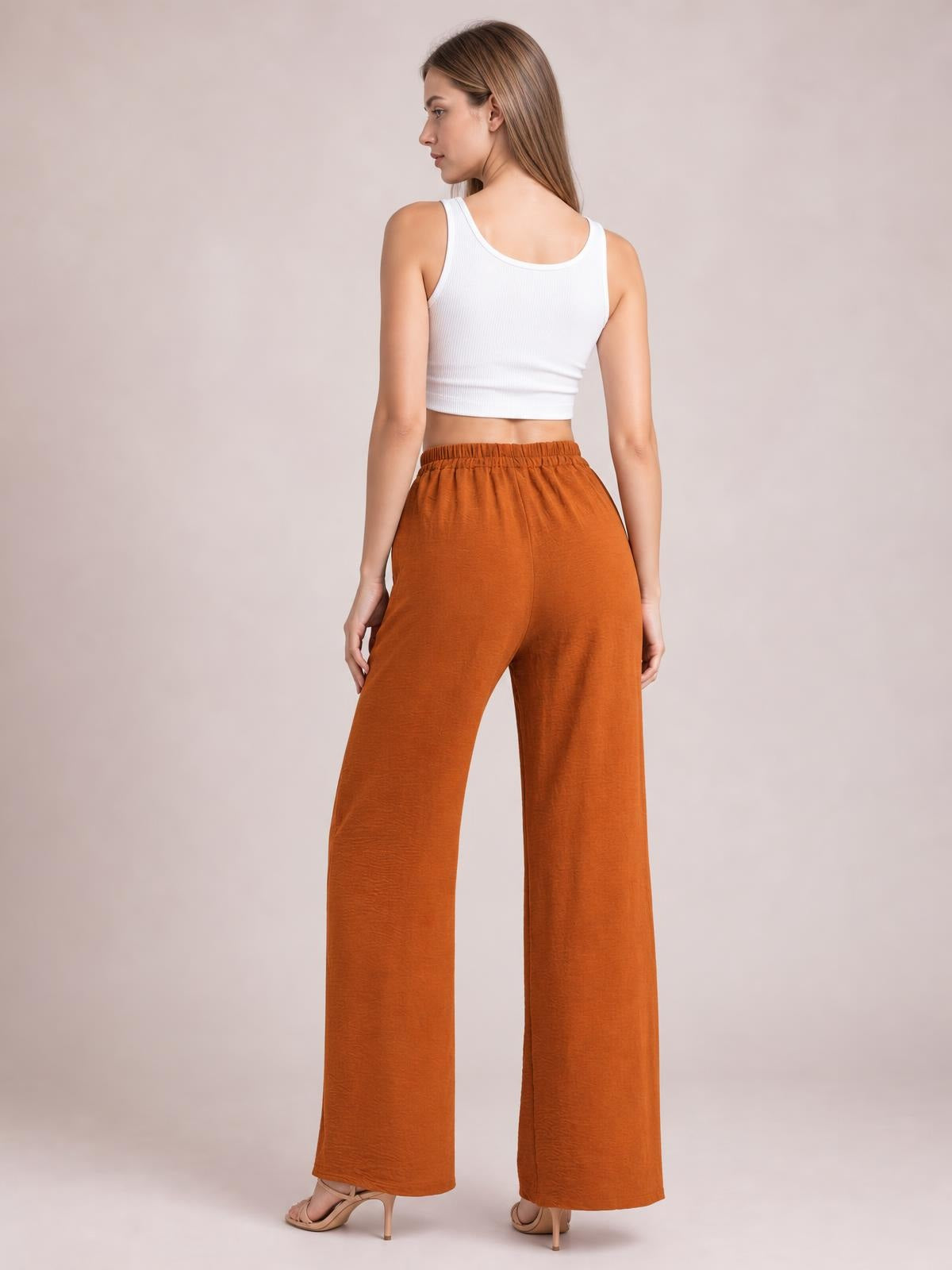 Model shown from behind wears rust-orange wide-leg drawstring pants with a gathered waistband, flowing silhouette, and full-length straight legs.