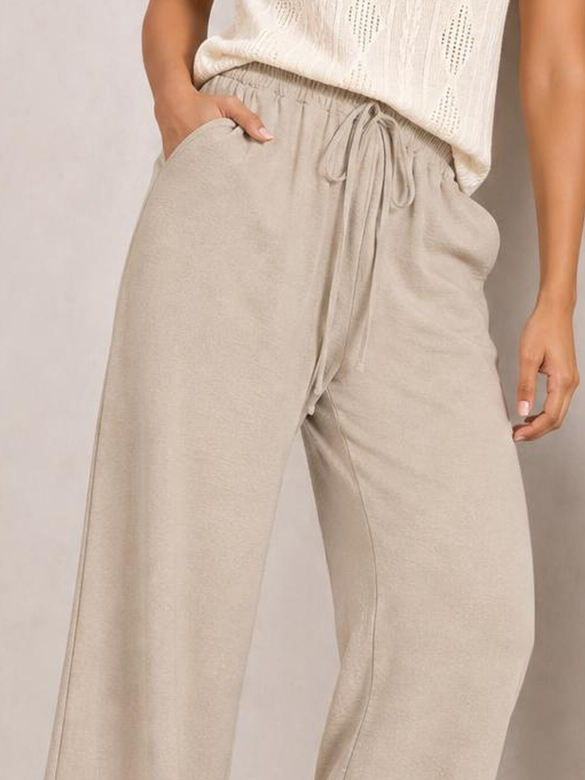 Model wearing beige wide leg drawstring pants with an elastic waistband, front tie, side pockets, and a relaxed flowy silhouette.