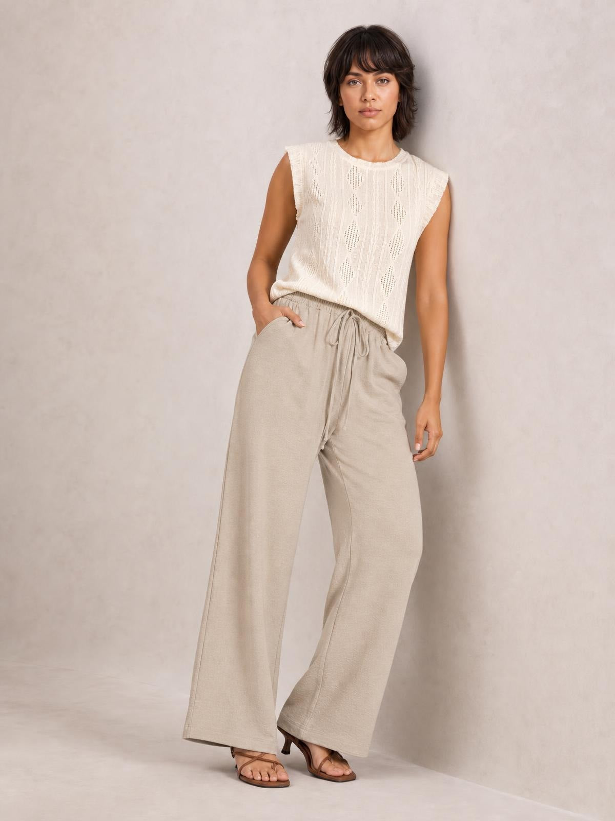 Model poses with one hand in the pocket wearing beige wide leg drawstring pants with a relaxed, flowy silhouette and elasticized waist.