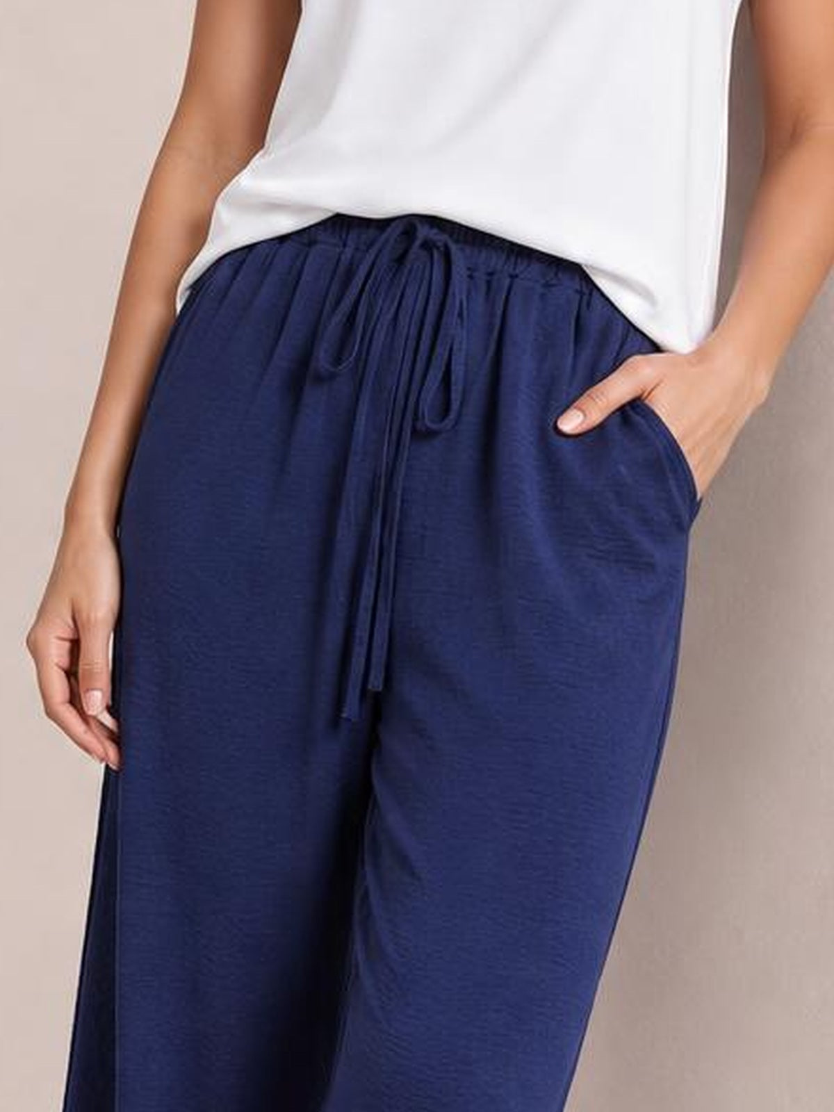 Model wearing navy wide leg drawstring pants with a relaxed flowy silhouette, gathered elastic waistband, long front tie, and side pockets.