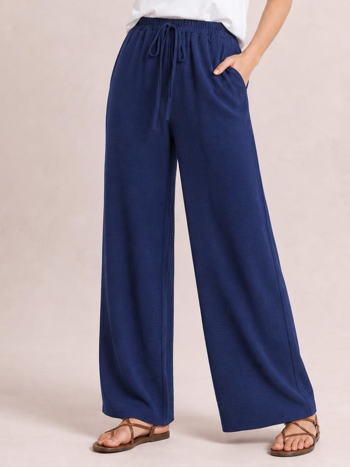 Model wearing navy wide leg drawstring pants with an elasticized waistband, flowing full-length silhouette, and one hand tucked into a side pocket.