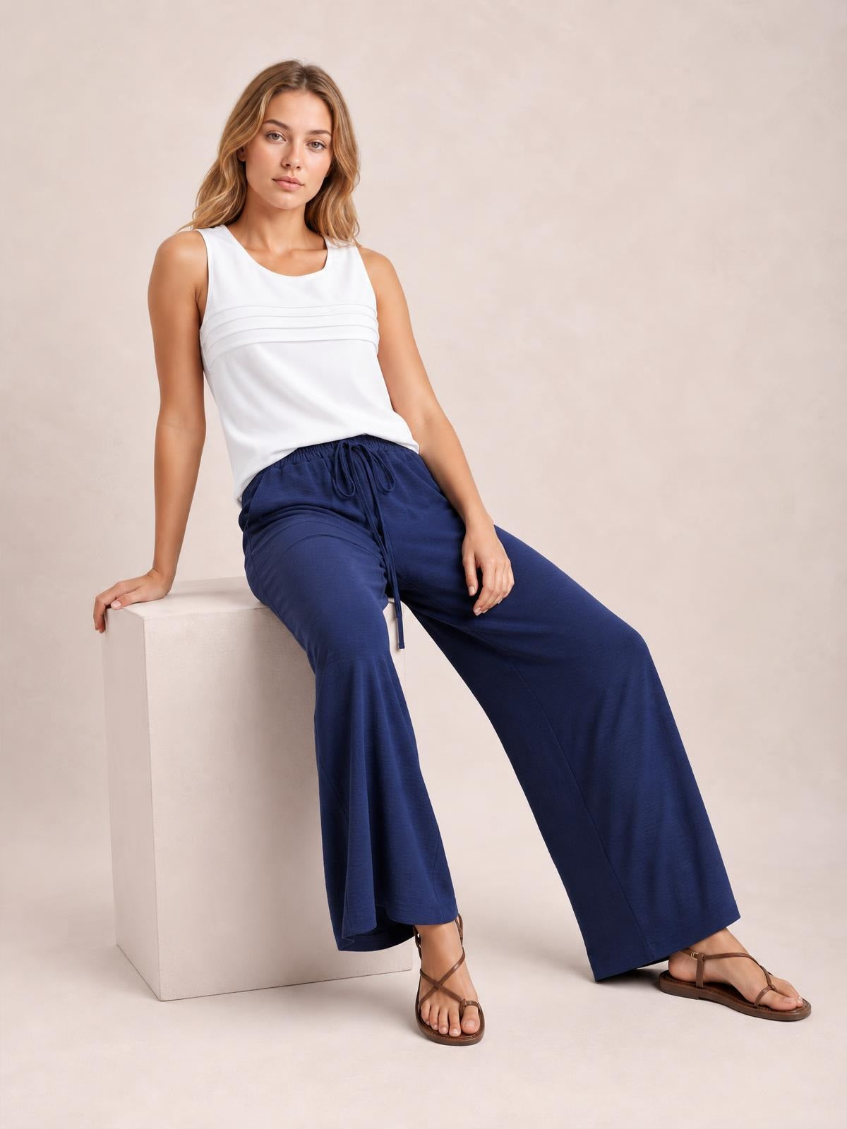 Model seated in navy wide leg drawstring pants with a relaxed, flowy silhouette, elastic waist, and visible front tie.