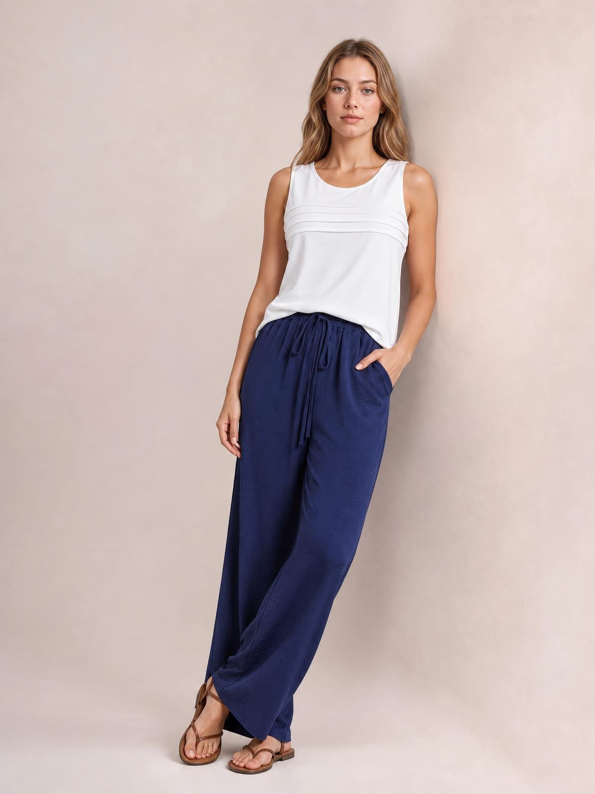 Model wears navy blue wide-leg drawstring pants with a flowy silhouette, gathered waistband, and relaxed fit, posing with one hand in a pocket.