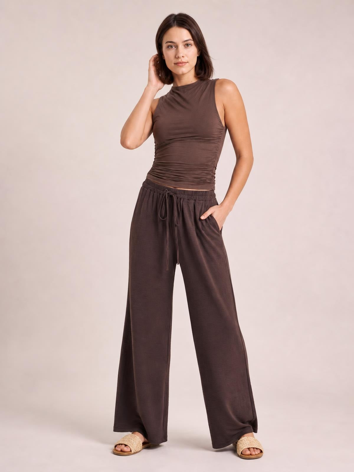 Model poses in dark brown wide leg drawstring pants with a relaxed, flowy silhouette, elastic waistband, front tie, and side pockets.