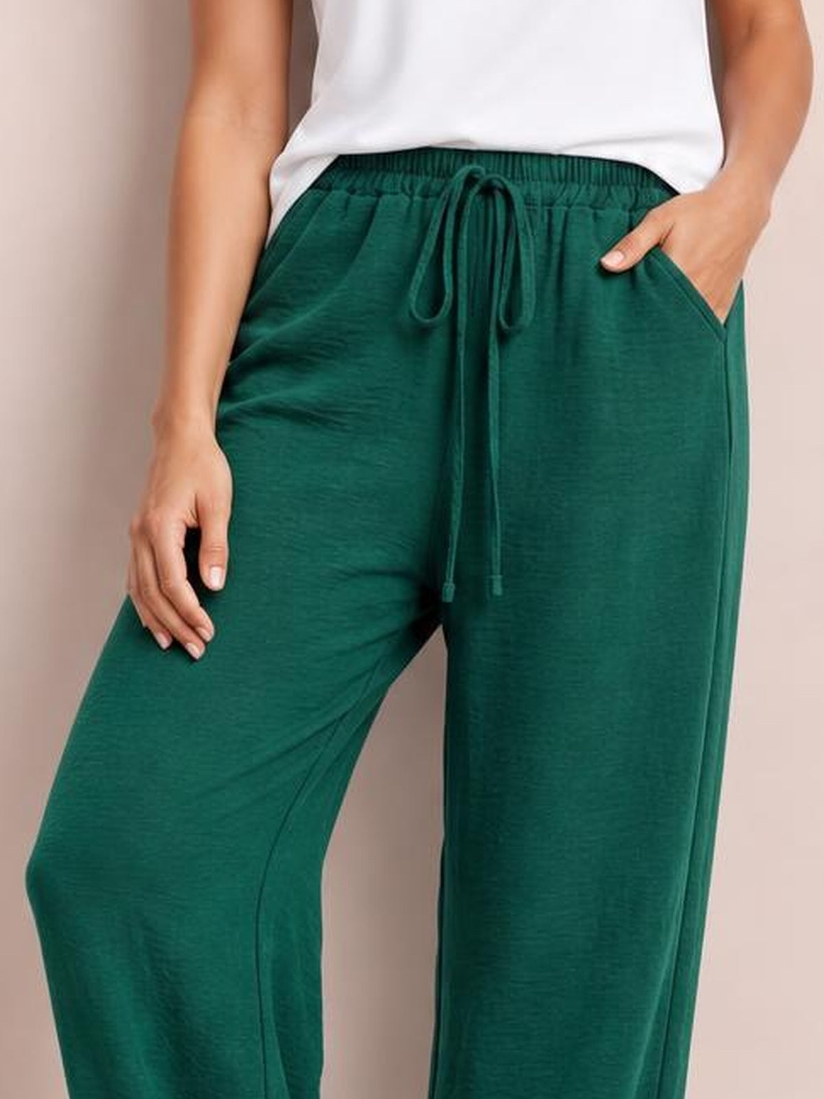 A model wears emerald green wide leg drawstring pants with an elastic waistband, front tie, relaxed flowy silhouette, and side pockets.