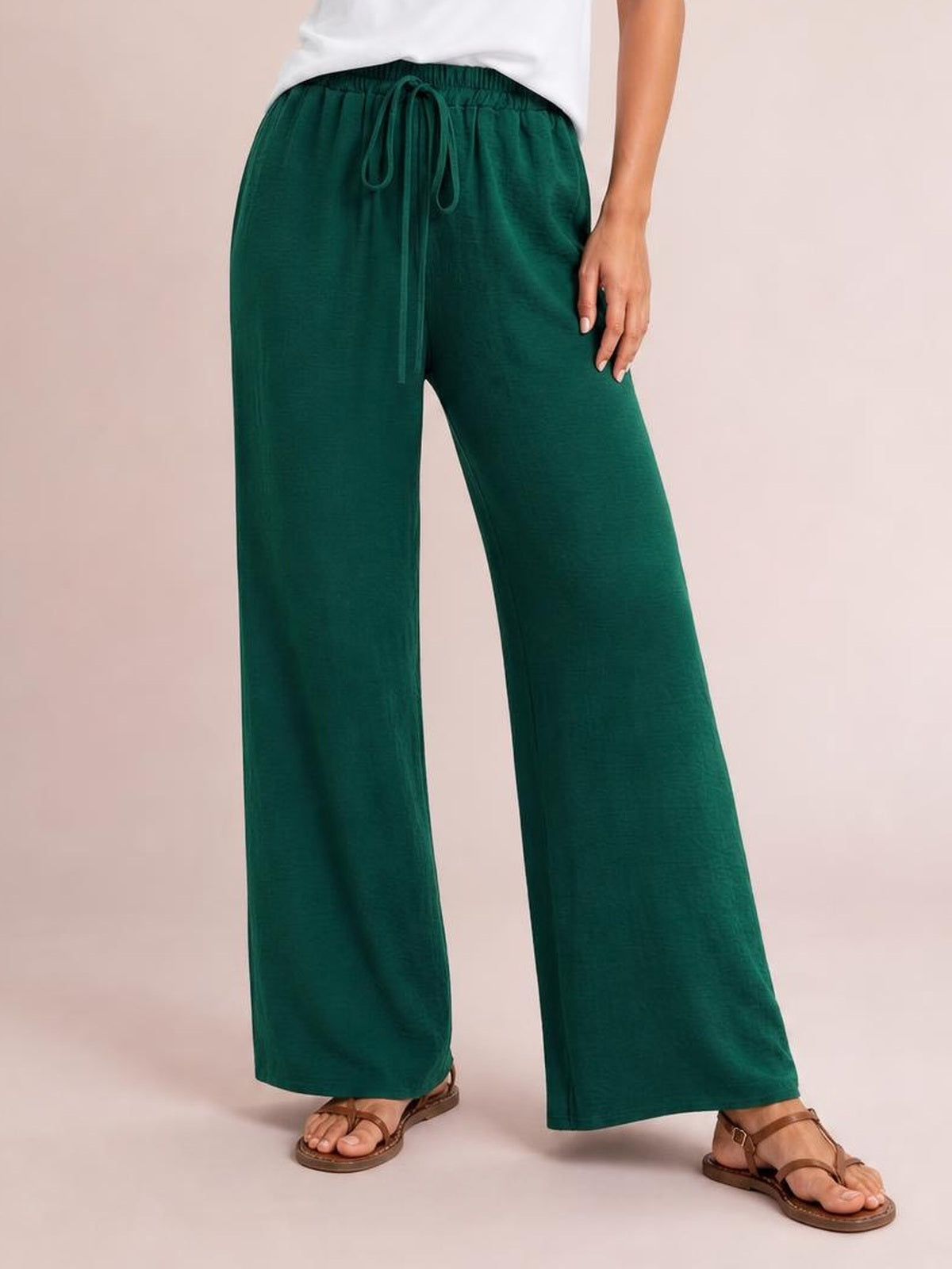 Model wearing dark green wide leg drawstring pants with an elastic waist, relaxed flowing silhouette, and ankle-length hems.
