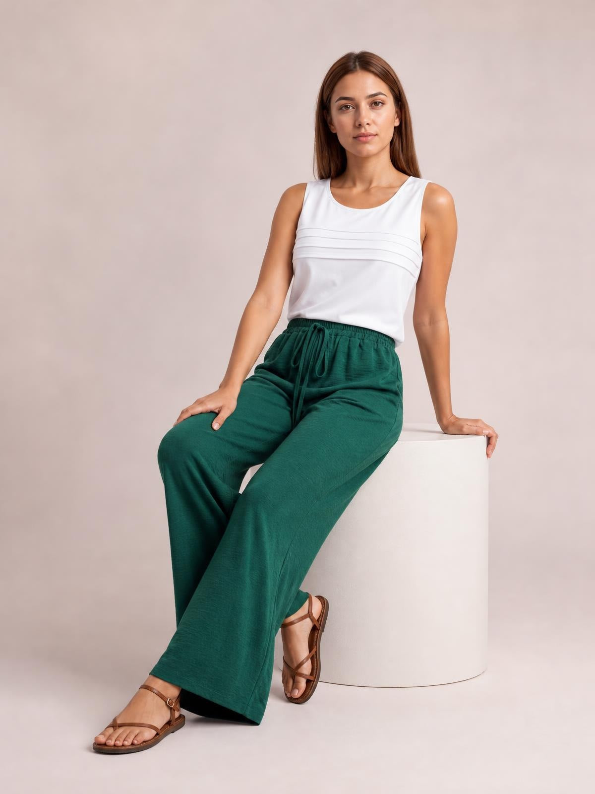 Model seated in deep green wide leg drawstring pants with a relaxed, flowy silhouette, elasticized waist, and visible front drawstring.