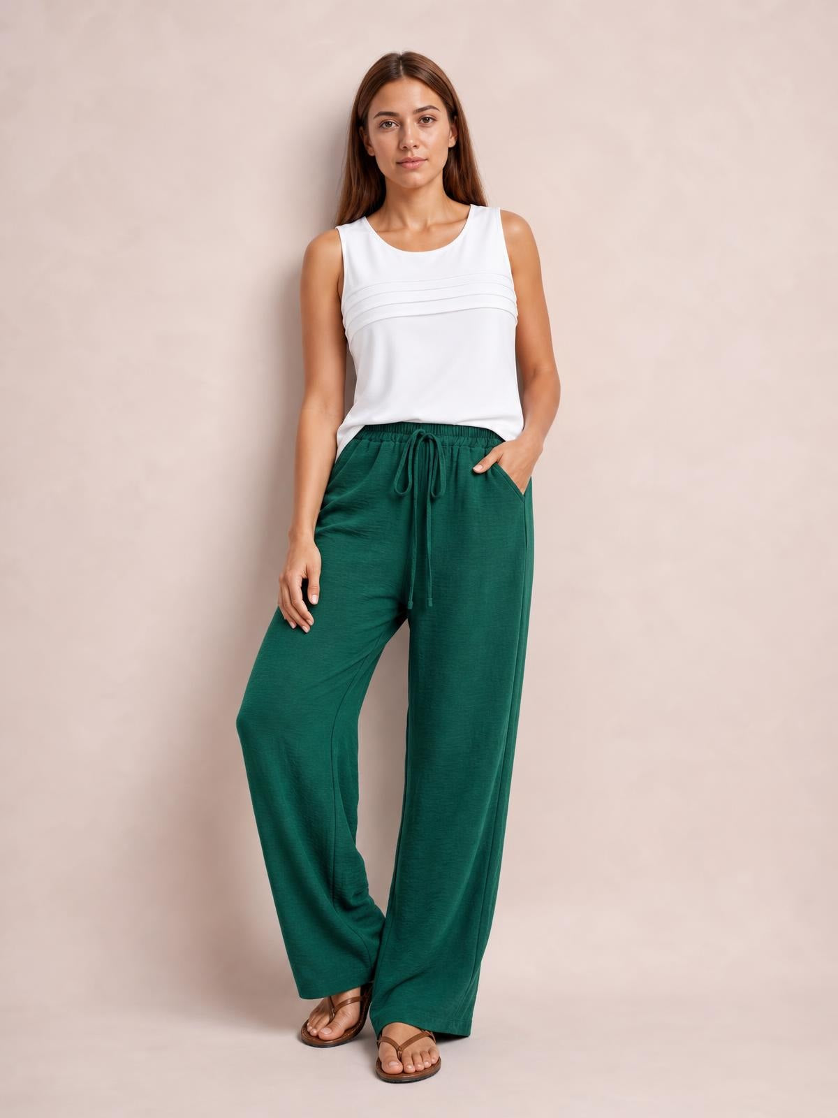 Model wearing emerald green wide leg drawstring pants with a relaxed flowy silhouette, elastic waistband, front tie, and side pockets.