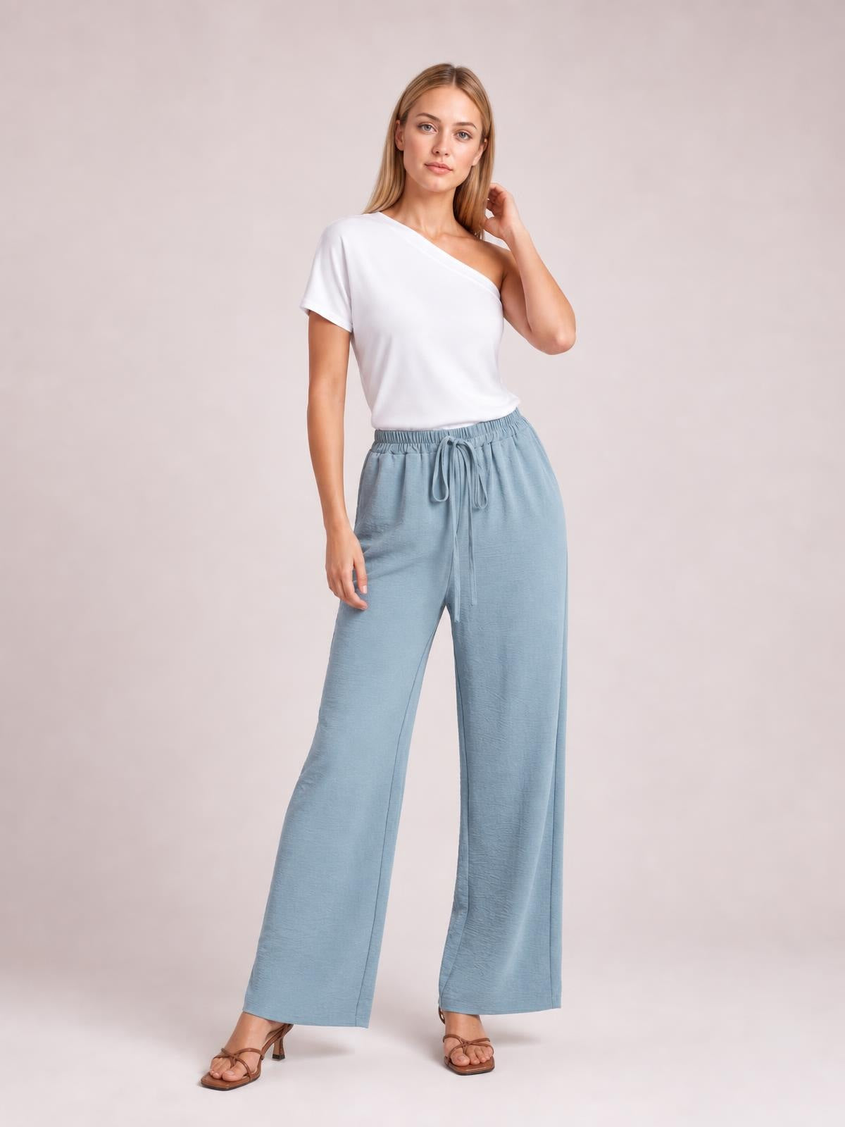 Model wearing light blue wide-leg drawstring pants with an elastic waistband and relaxed, flowy silhouette, paired with a white one-shoulder top.