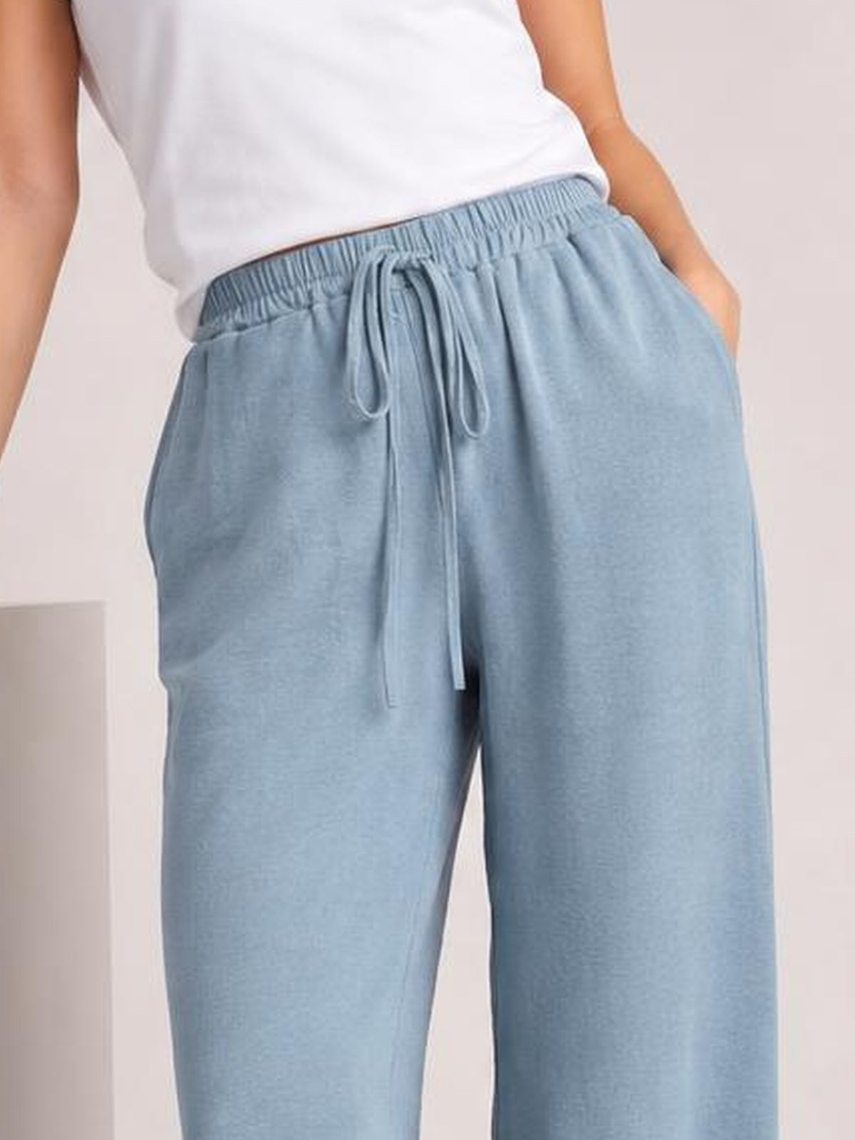 Model wearing light blue wide-leg drawstring pants with an elastic waistband, relaxed flowy silhouette, and hands in the side pockets.
