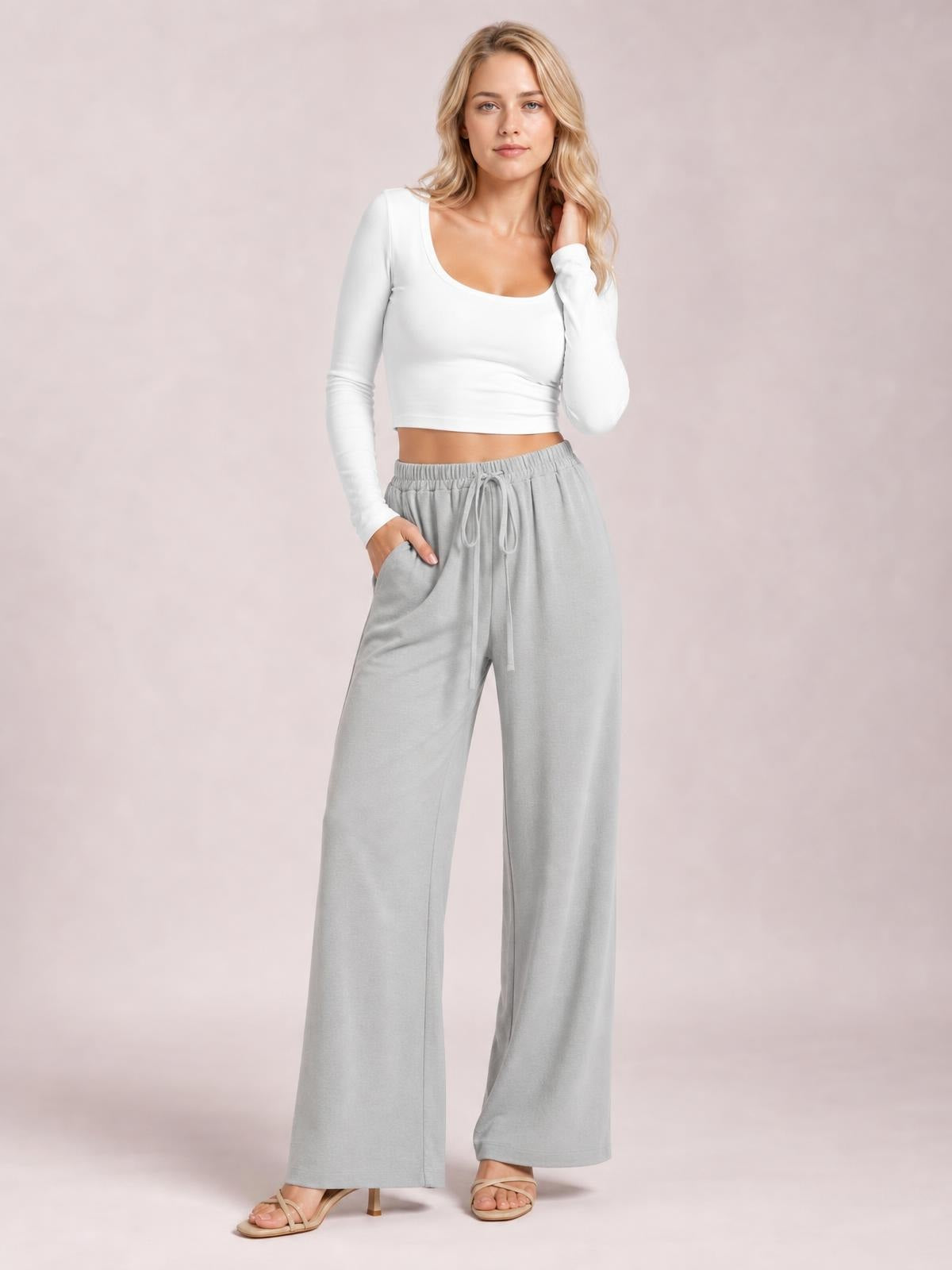 Model poses in light gray wide leg drawstring pants with an elasticized waist, flowing full-length silhouette, and side pockets.