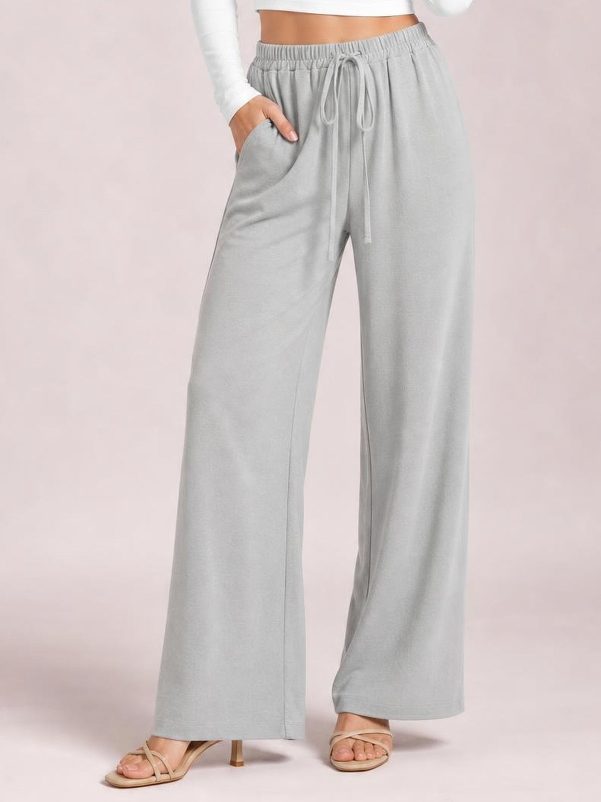Model wearing light gray wide-leg drawstring pants with an elastic waist, front tie, side pockets, and a relaxed flowy silhouette.