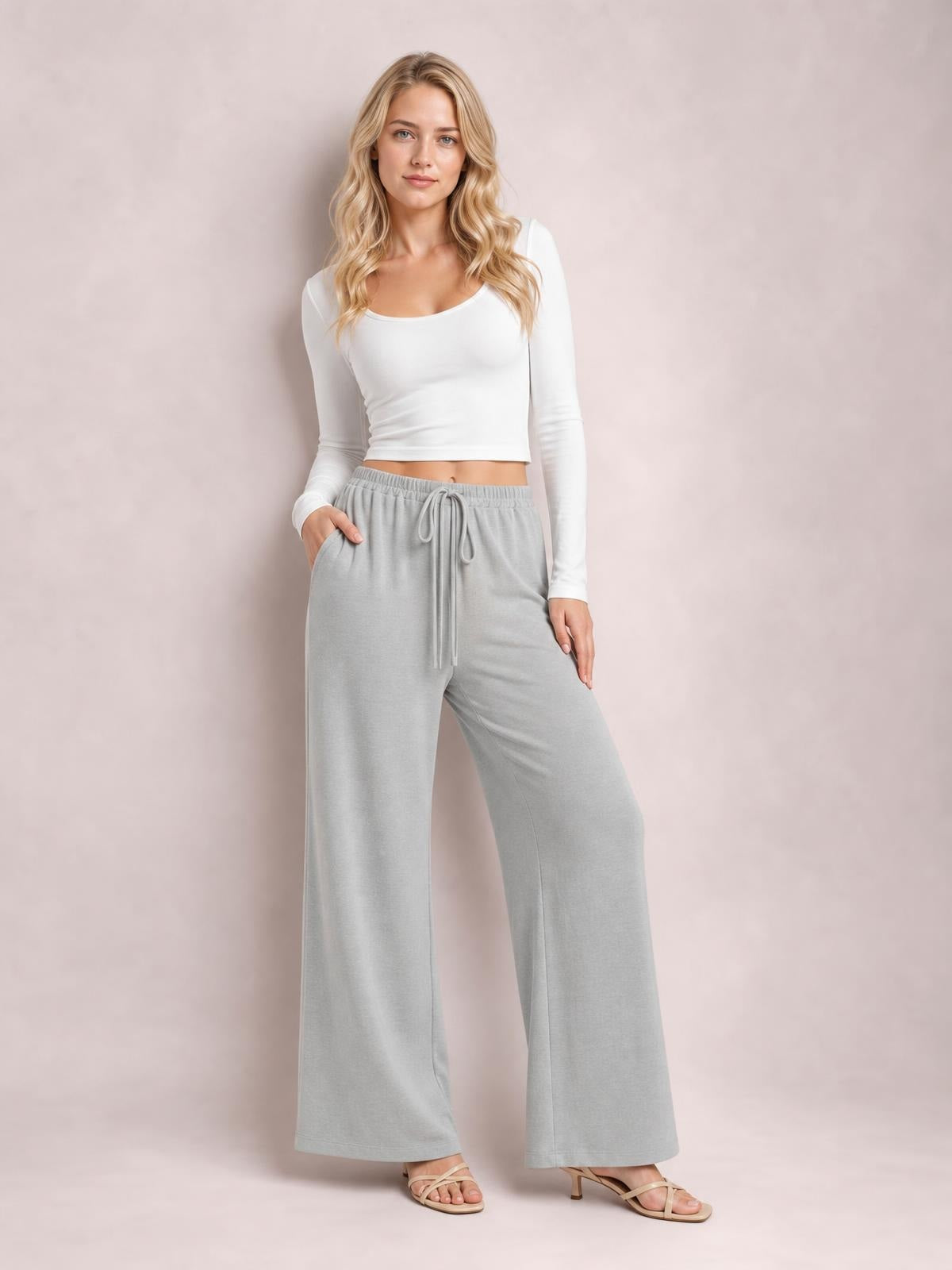 A model poses in light gray wide-leg drawstring pants with a relaxed, flowy silhouette, elastic waistband, and long straight legs.