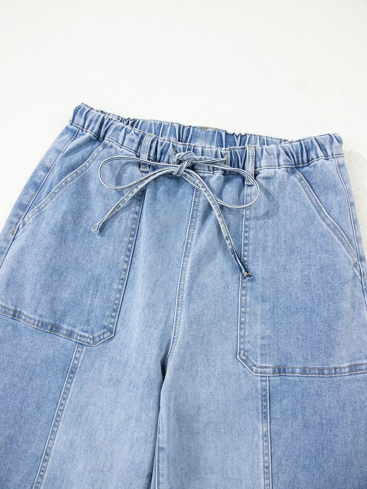 Light blue wide-leg jeans shown flat with an elasticized drawstring waist, roomy silhouette, stitched seams, and large patch pockets.