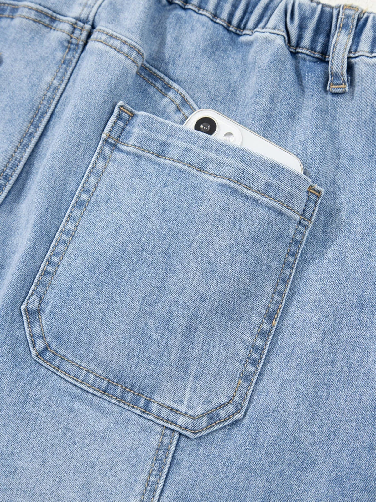 Close-up of light blue jeans showing a large pocket with reinforced double stitching, a structured waistband, and a belt loop.