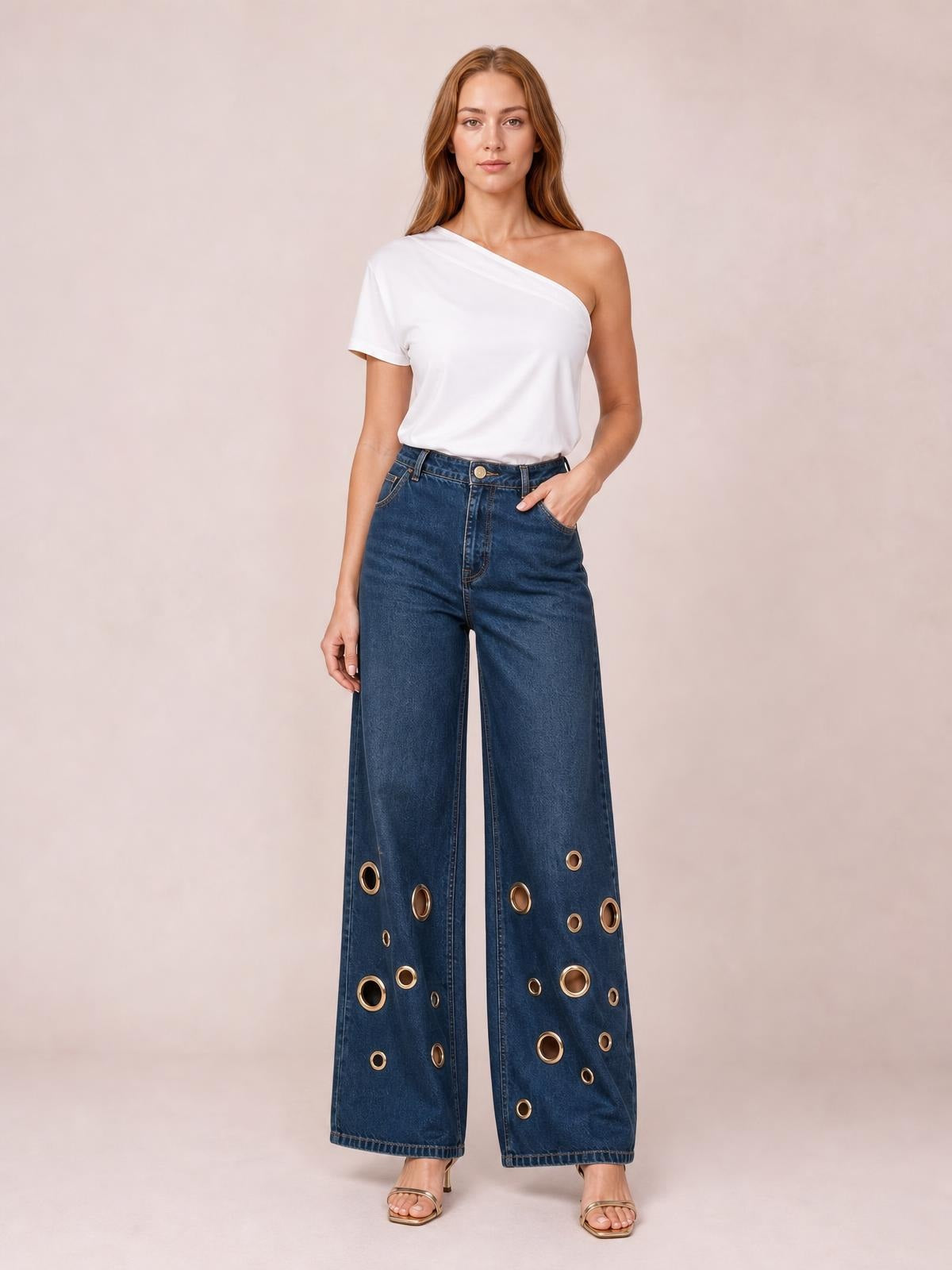 Model wearing dark blue wide-leg jeans with a high-rise waistband, front pockets, straight seams, and gold-tone eyelet details throughout the lower legs.