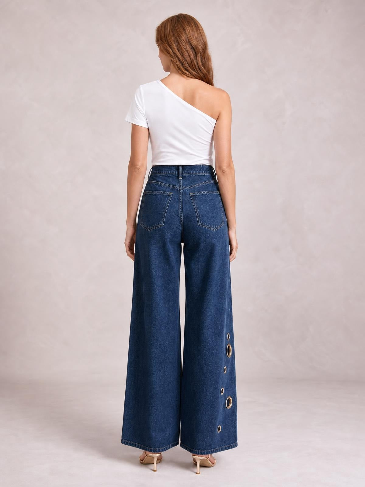 Model shown from the back wearing dark blue wide-leg jeans with a high waist, back pockets, and eyelet details along the outer leg.