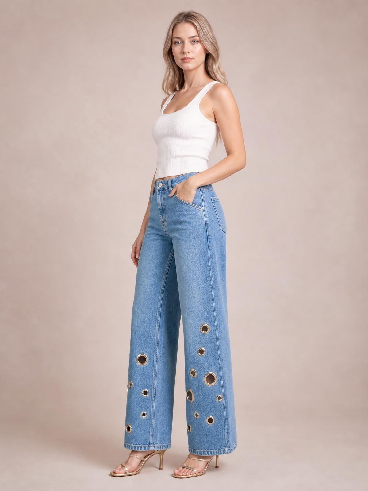 Model poses in light blue wide leg jeans with a high-rise fit, front pockets, structured seams, and multiple metal eyelet details along the legs.