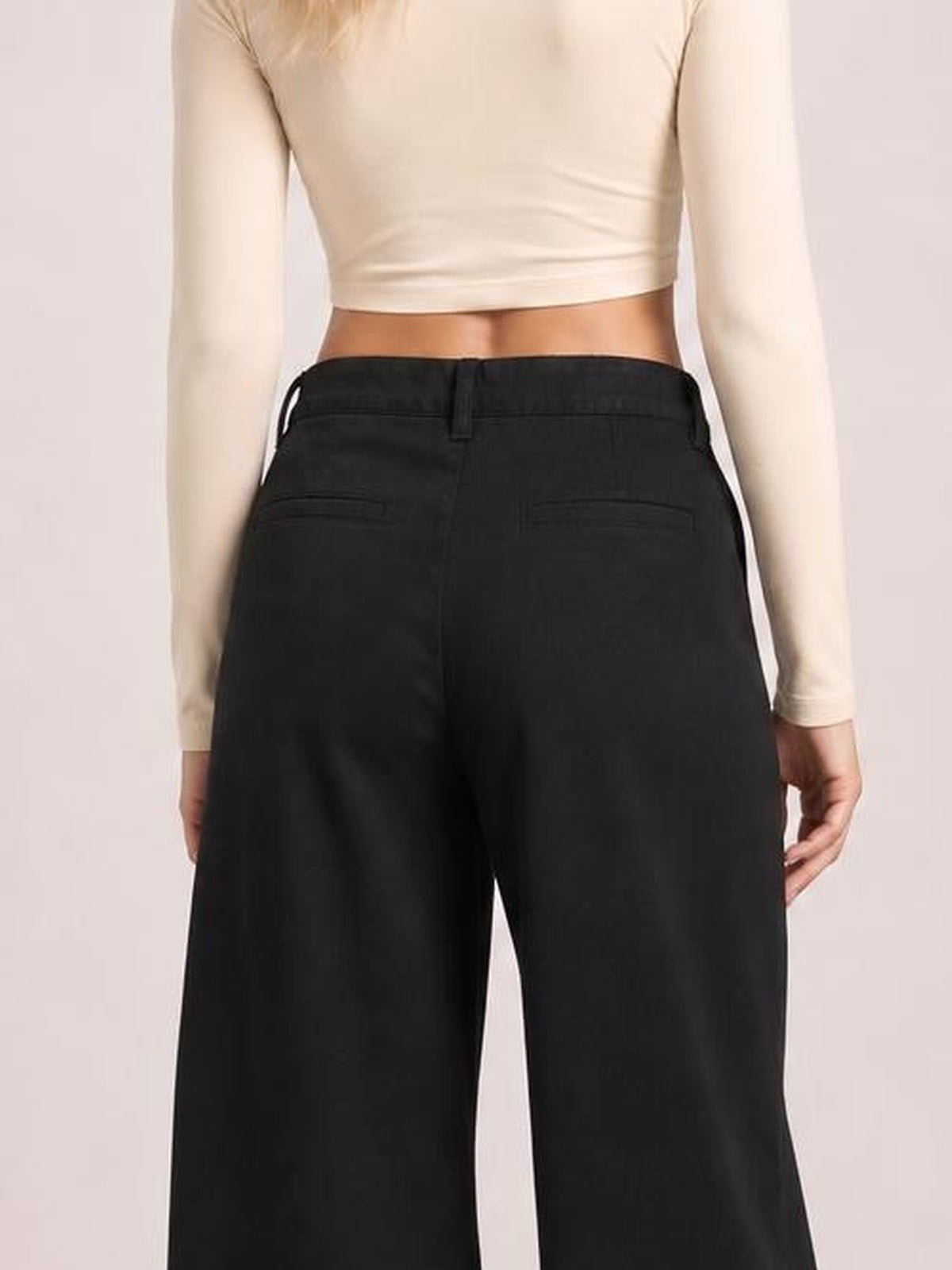 Model shown from behind wearing black wide-leg jeans with belt loops, a structured waistband, back pockets, and a relaxed full-leg silhouette.