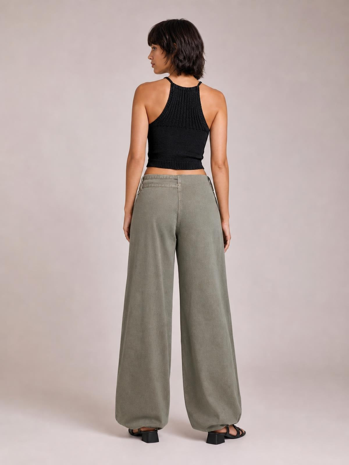 Model shown from behind wears gray wide leg jeans with pockets, a structured waistband, and a relaxed full-length silhouette, standing in black heeled sandals.