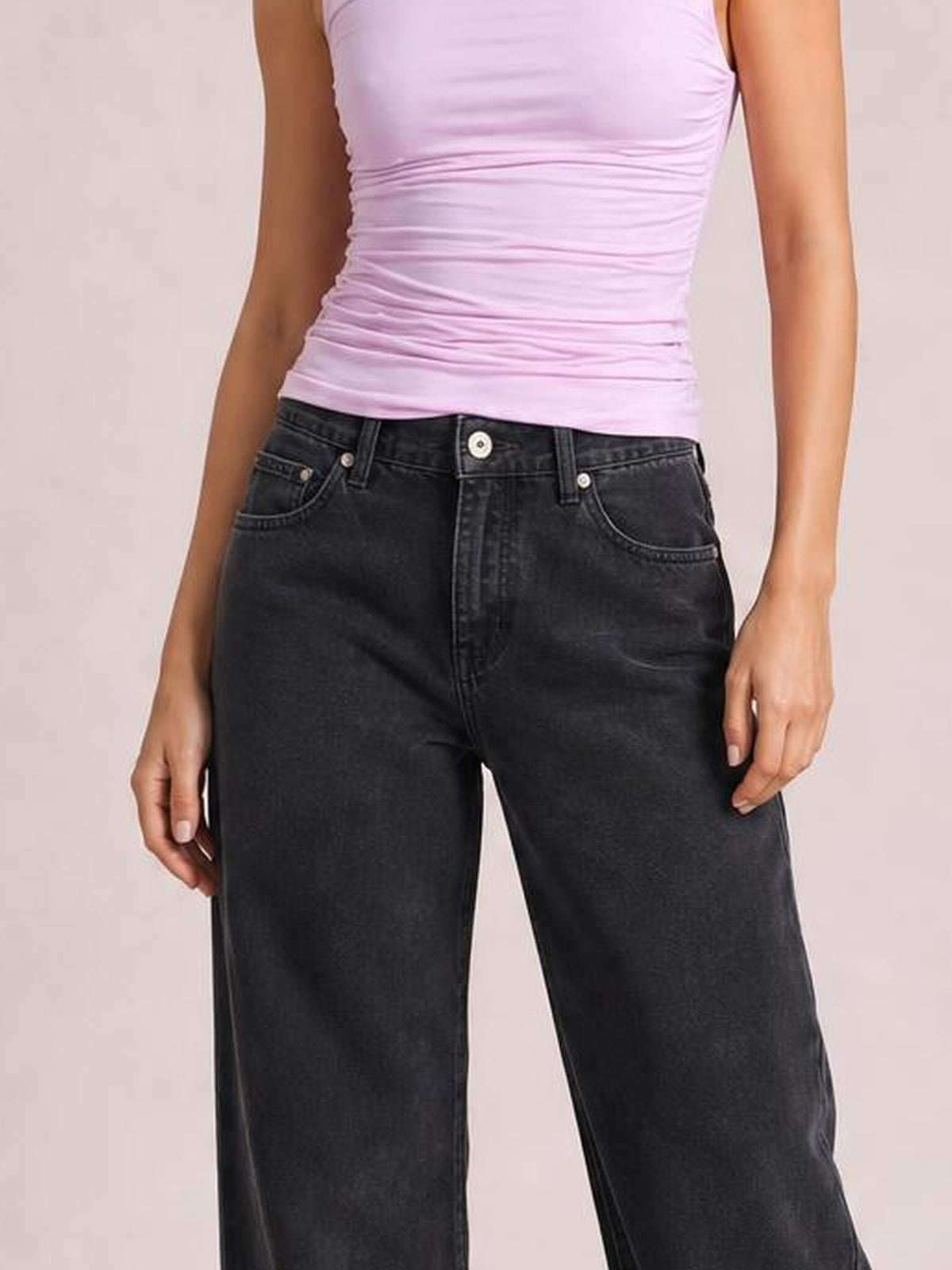 A model stands with hands at her sides, wearing dark black wide-leg jeans with a button closure, belt loops, and visible front pockets.