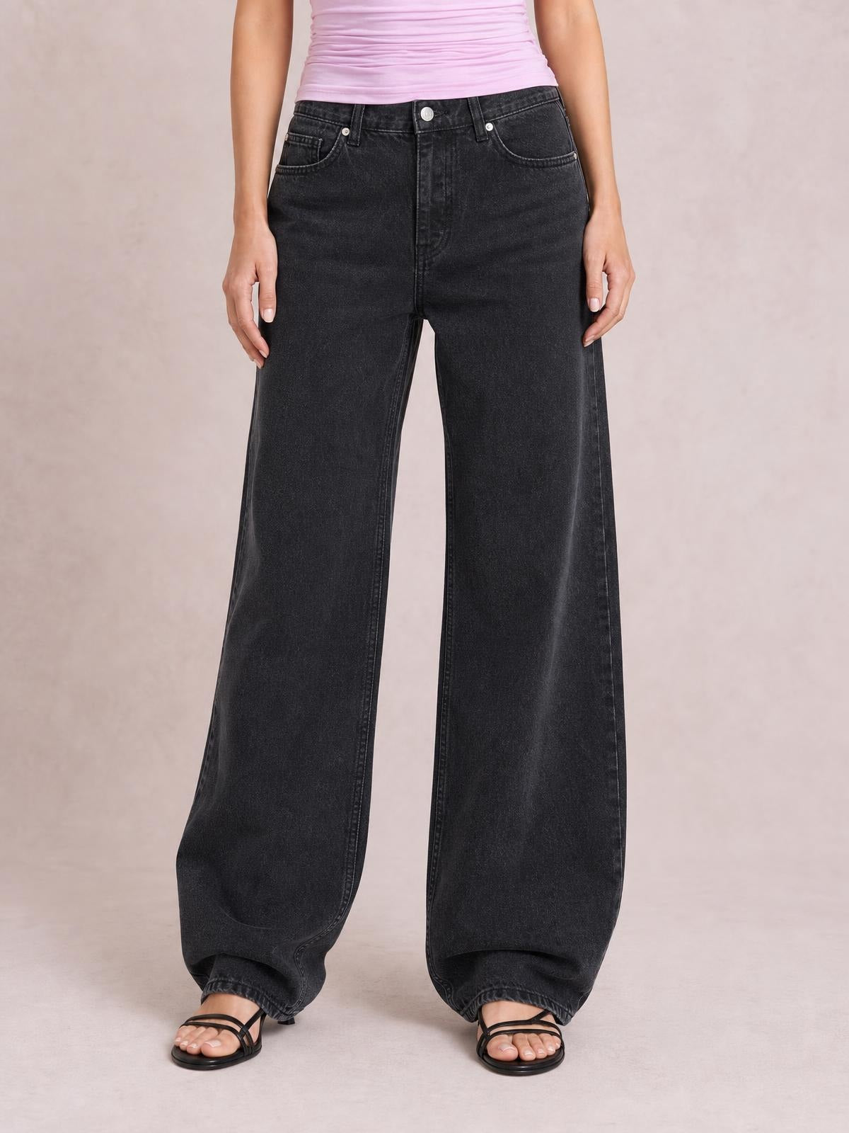 A standing model wears black wide-leg jeans with front pockets, belt loops, a button closure, and a long, relaxed silhouette.